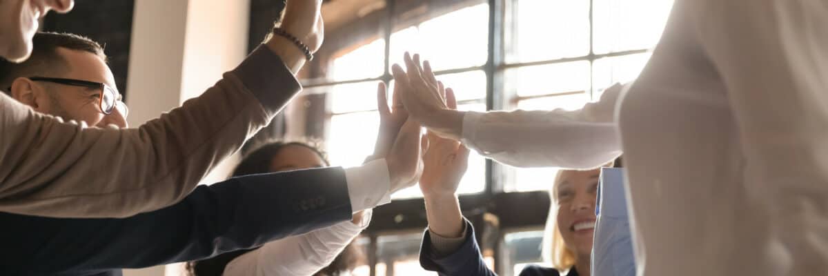 Overjoyed older and younger teammates joining hands in air, giving high five, celebrating shared company success in business meeting. Happy diverse colleagues coming to common decision, showing unity.